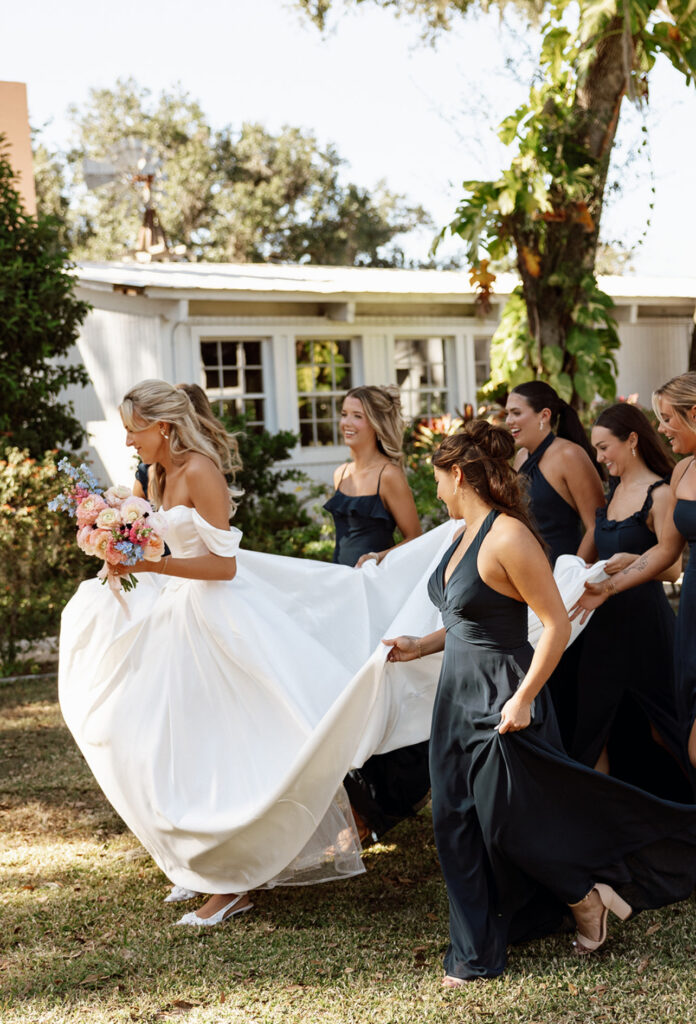 Bride running with her bridesmaids during a Charleston wedding, showcasing permanent jewelry from Coastal Chains.