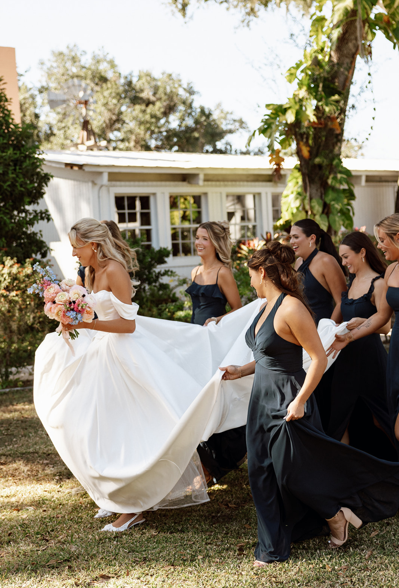 Bride running with her bridesmaids during a Charleston wedding, showcasing permanent jewelry from Coastal Chains.